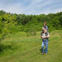 a man with a boy on his shoulders walking on a wide path in a field