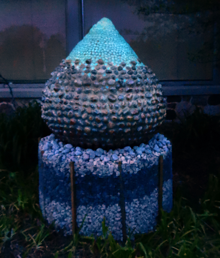 Tear-drop shaped sculpture made of glow-in-the-dark stones glowing at dusk