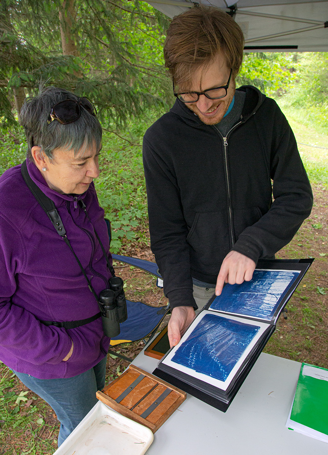 Artist in residence Andrew Musil showing a visitor examples of cyanotype images he's made on site 