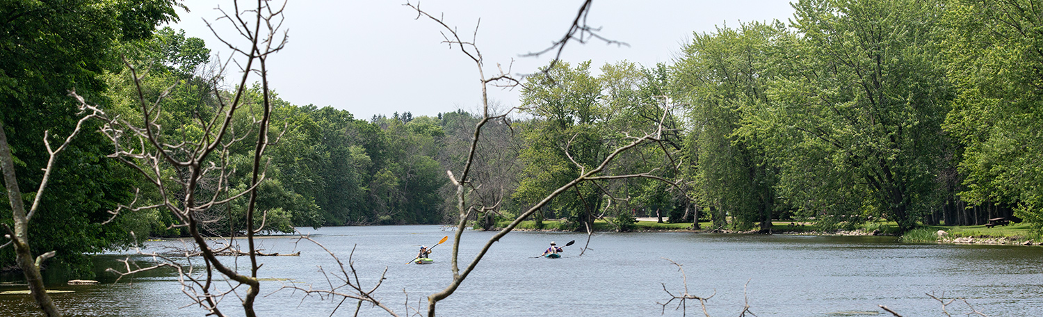 two kayakers in the middle of the Milwaukee River with wooded shores