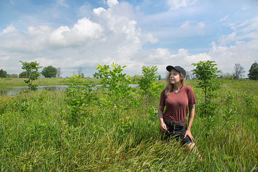 The artist standing in high grass on the prairie at Forest Beach Migratory Preserve with a pond and thunderhead in the background