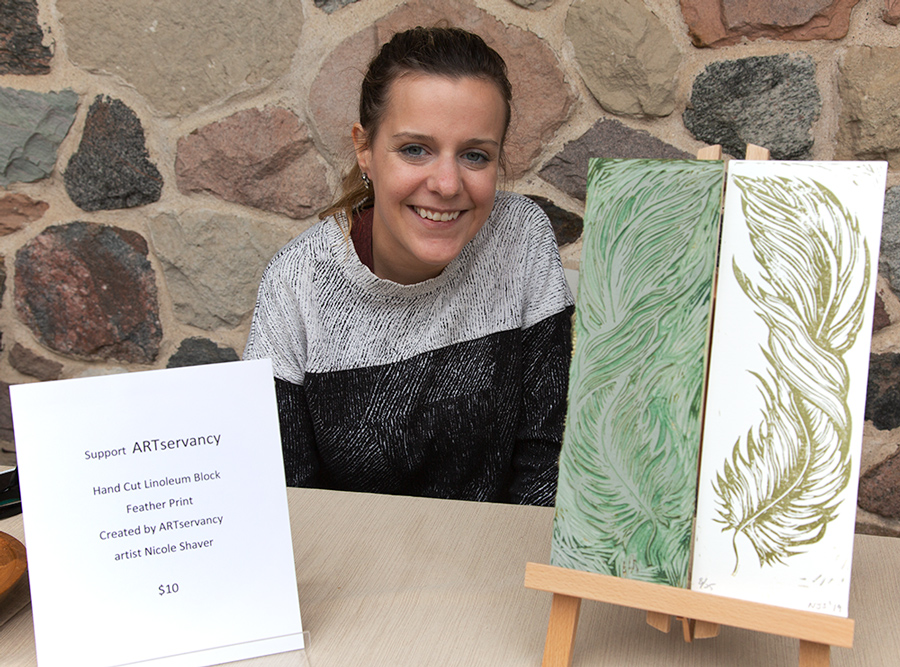 a smiling young woman artist with linoleum block cut and print sitting at a table