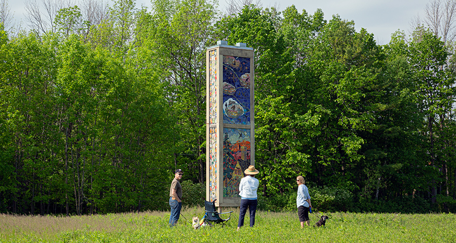 three people around artistic chimney swift tower with ceramic murals on it