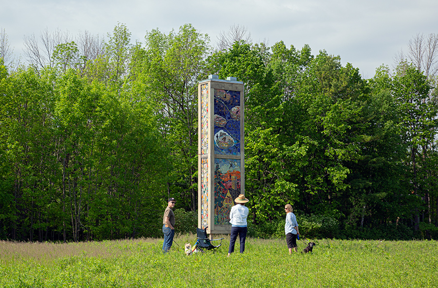 three people with dogs in front of swift tower art installation