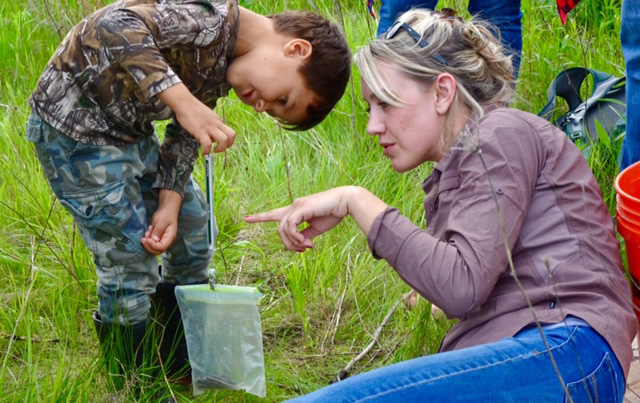 Conservation Biologist Julia Robson shows a boy how to measure the weight of a snake using a plastic bag