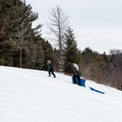 a boy and a man pulling sleds up a snowy hill