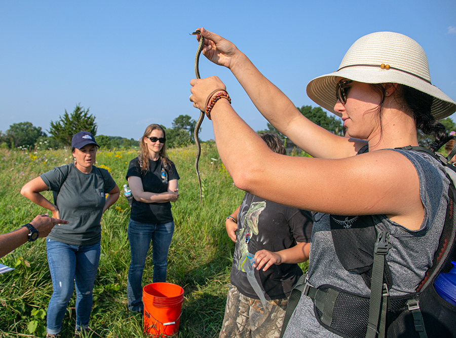 A woman in a hat holds up a garter snake as others look on