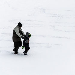 a man holding a boy's shoulders as they step out letters in the snow