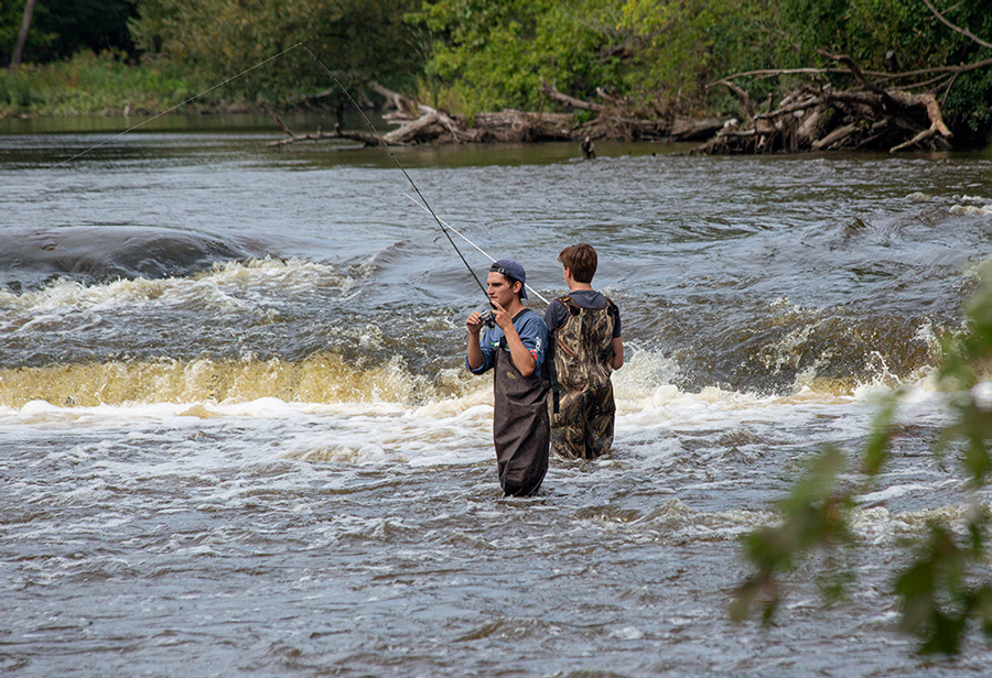 two young men in hip waders fishing below the falls in the Milwaukee River