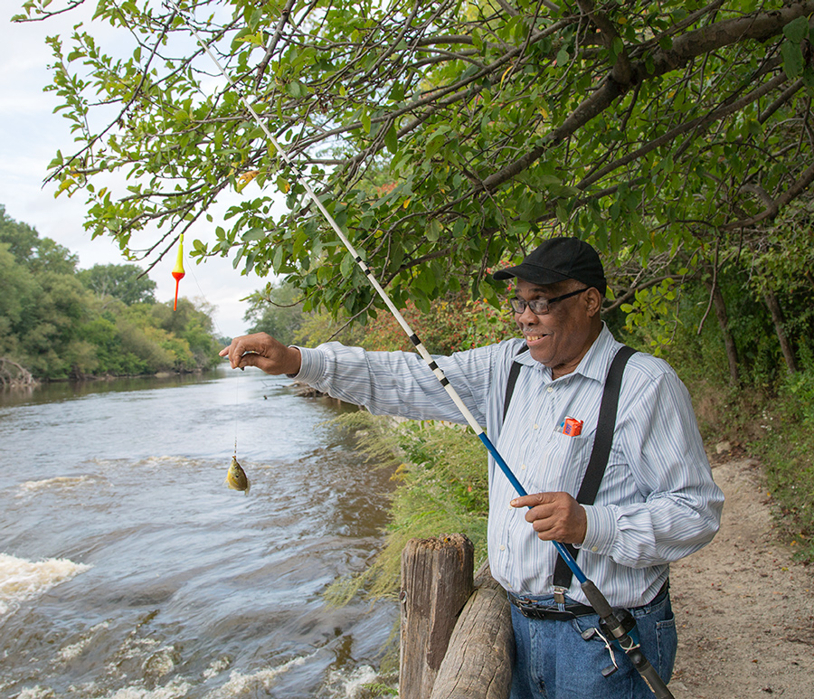 man holding up a fishing rod with a small bluegill attached, next to the Milwaukee River