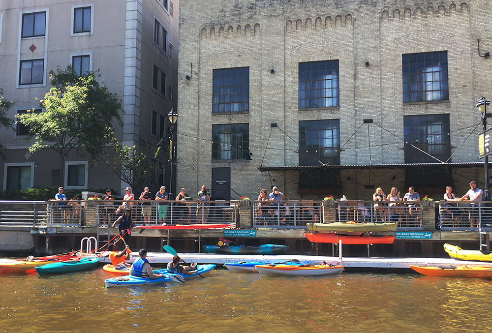 Kayaks docking and people lining the river walk at Lakefront Brewery on the Milwaukee River.