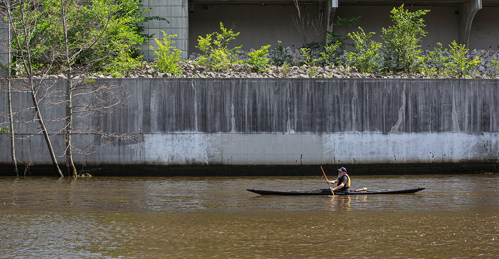 A kayaker paddling next to a concrete flood wall on the Milwaukee RIver