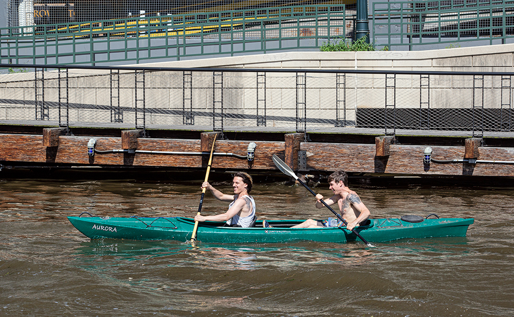 two young men in a two-person kayak next to the Riverwalk on the Milwaukee River