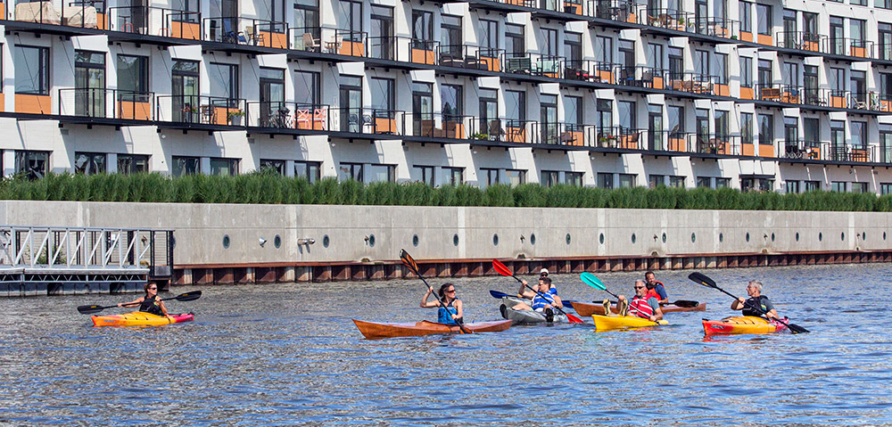 a group of kayaks paddling on the Milwaukee River next to a condo complex