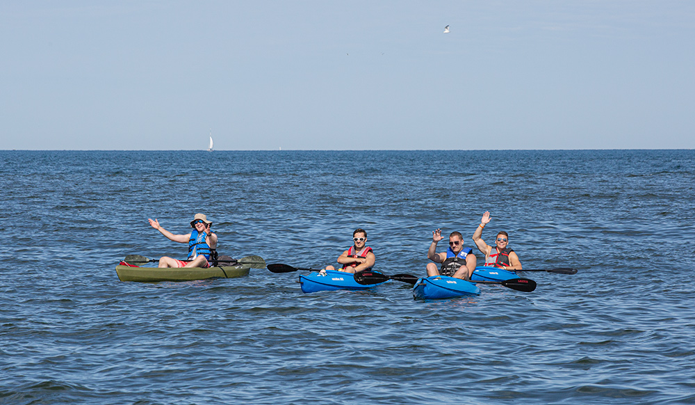 four men in kayaks floating out in the middle of Lake Michigan and waving