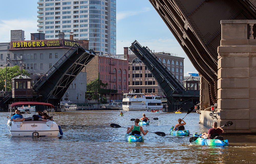 kayaks and a motorboat passing under raised drawbriges in downtown Milwaukee