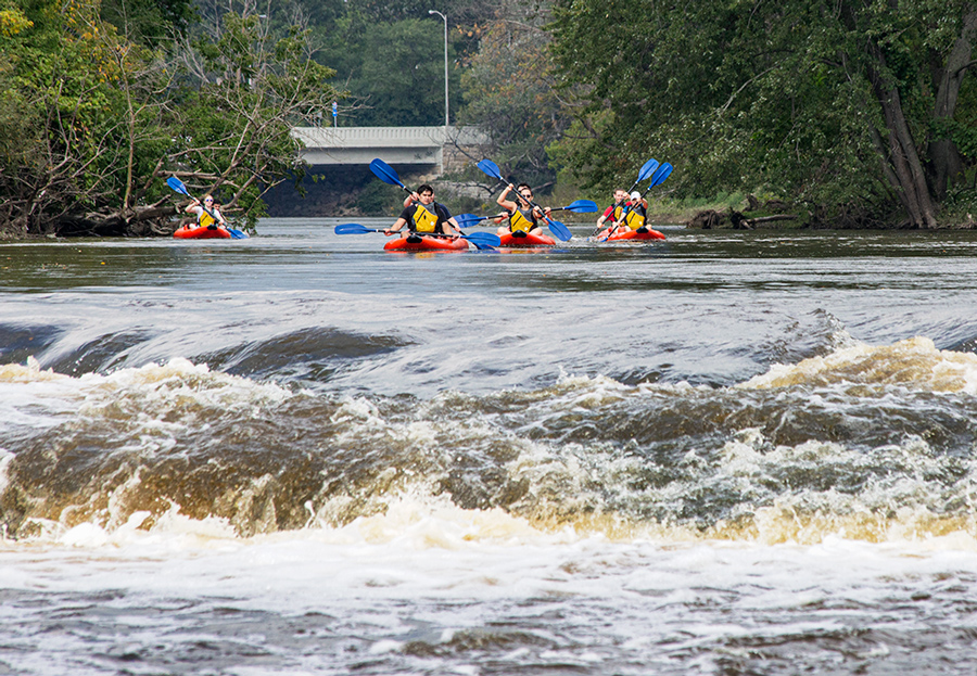 four red rubber rafts on Milwaukee River approaching falls