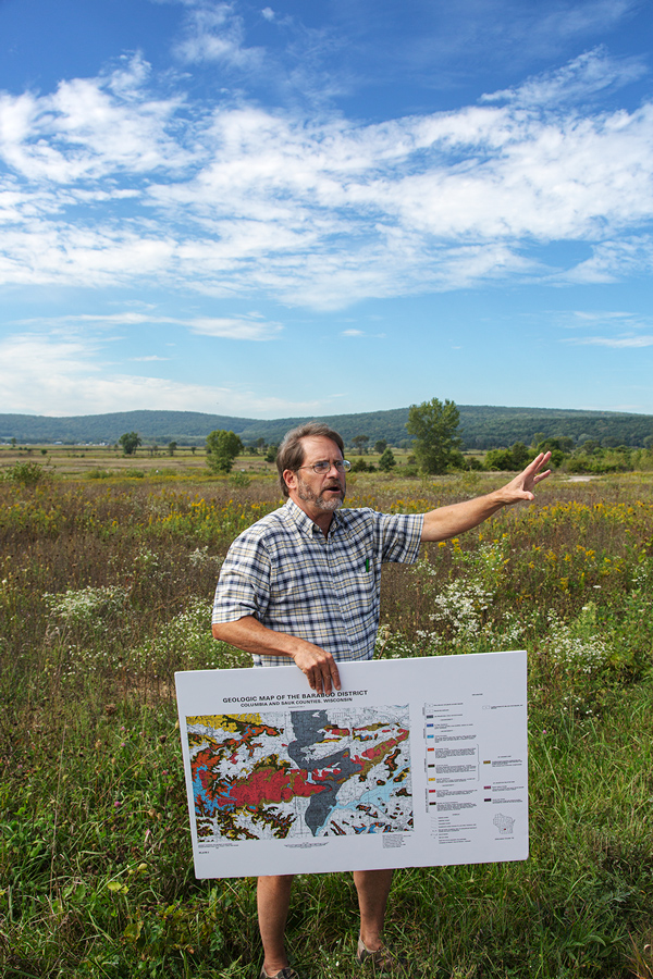 A man with a graphic map standing on a prairie with a low mountain range in the background