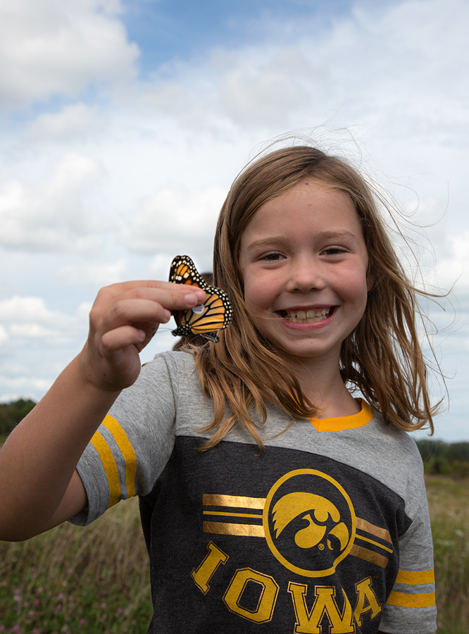 girl with a big smile holding a tagged monarch butterfly by the wings