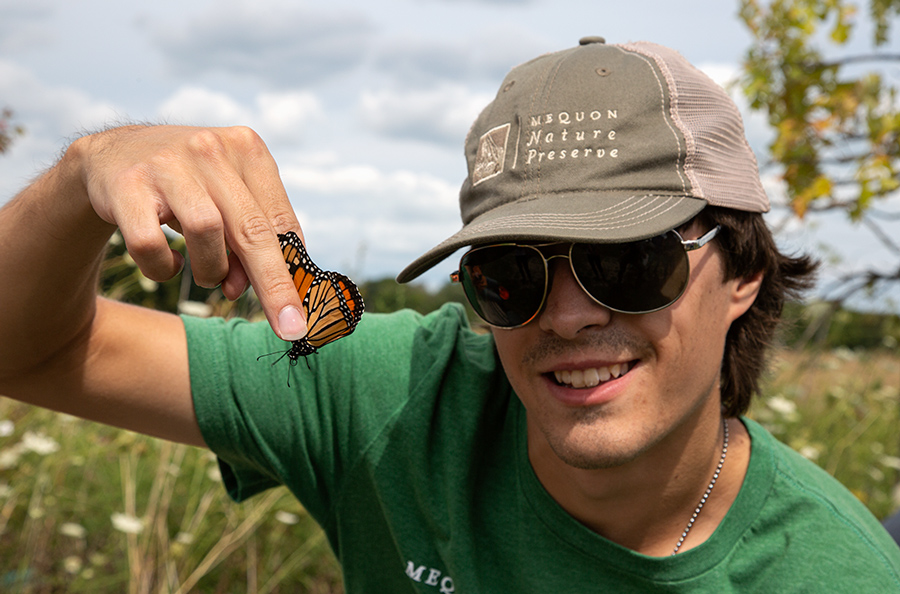 a man with a baseball cap and sunglasses holding a monarch butterfly