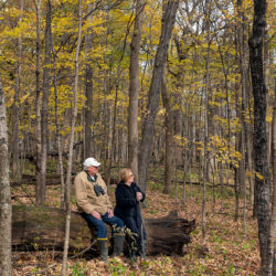 two people sitting on a log in the woods