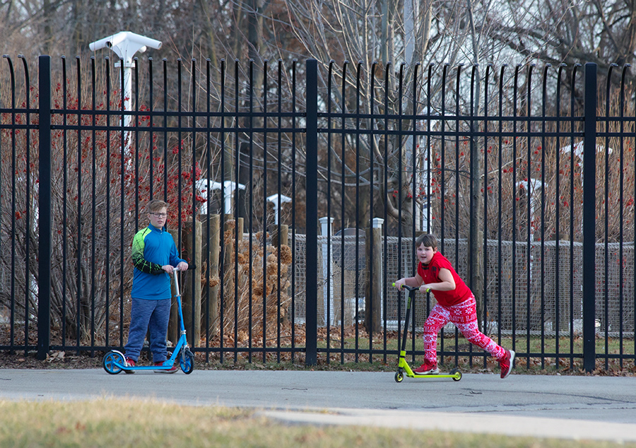 two boys on scooters in front of a fence