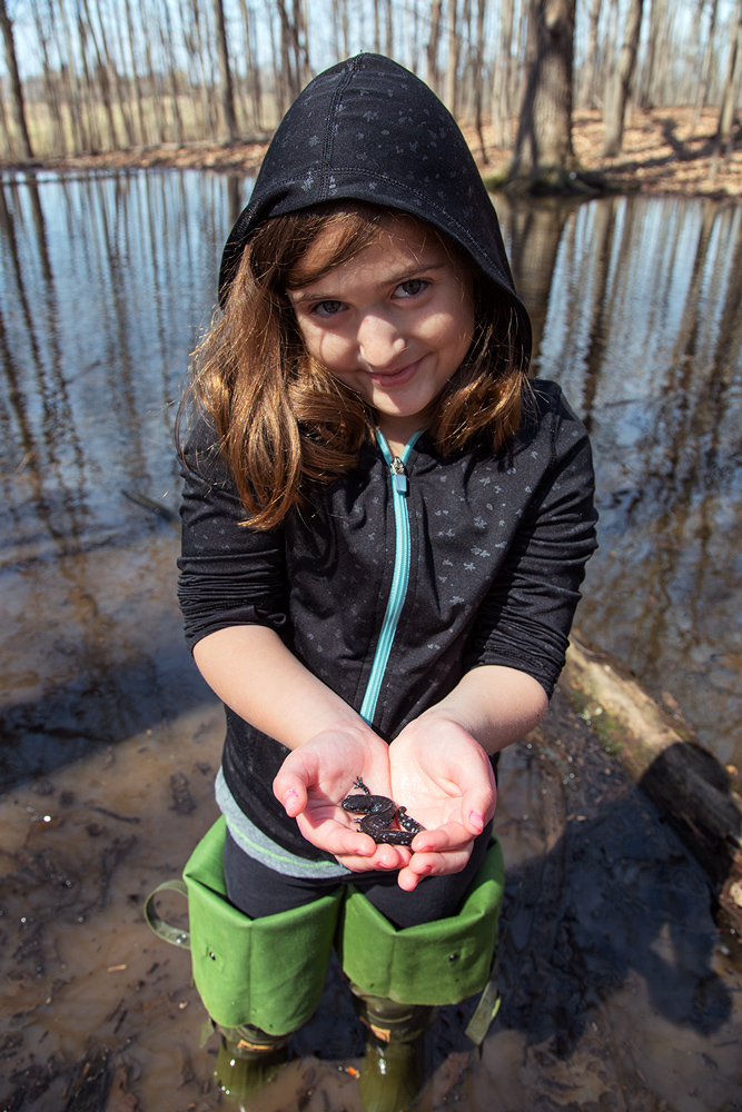 a young girl holding a salamander at a pond in Barloga Woods