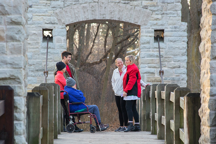 Several people, including one in a wheelchair, greeting each other on a foot bridge