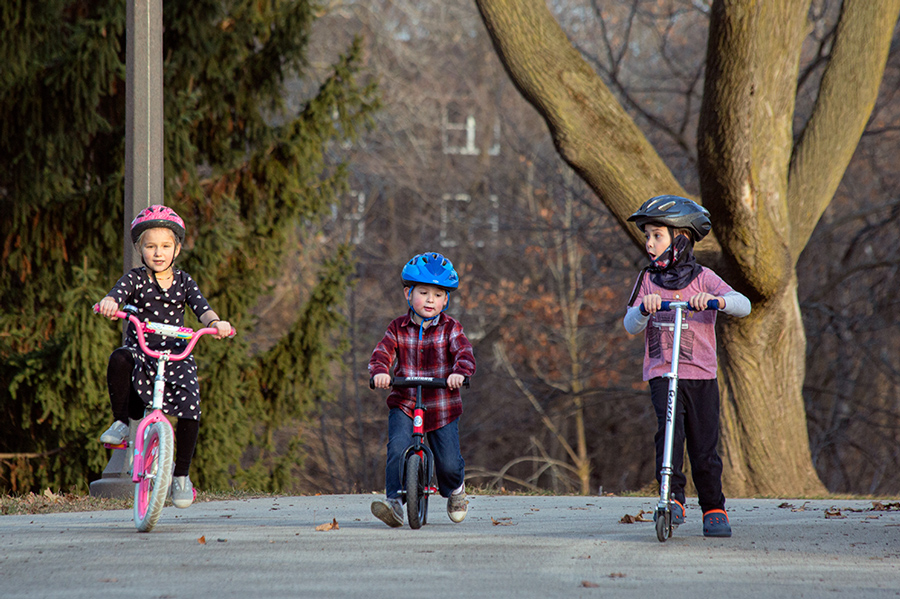 three young children, two on bikes and one on a scooter