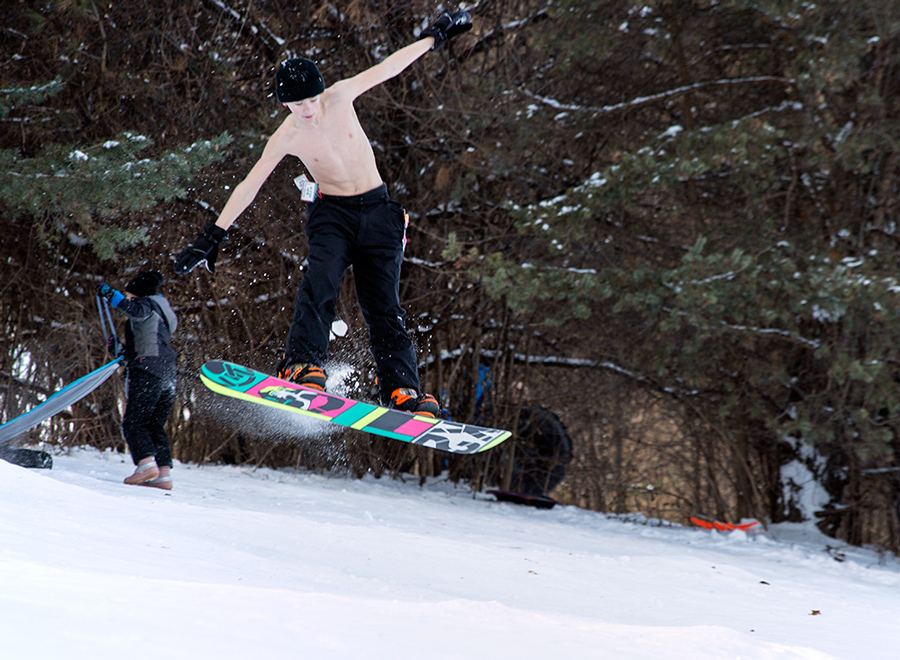 shirtless boy doing an aerial jump on a snowboard