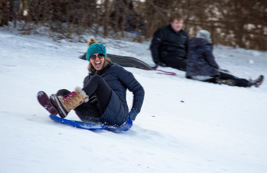 young woman screaming with joy as she sleds down a hill