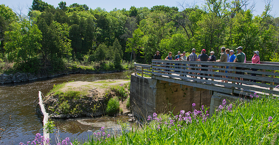 Tour group on pedestrian bridge overlooking former dam site on Milwaukee River