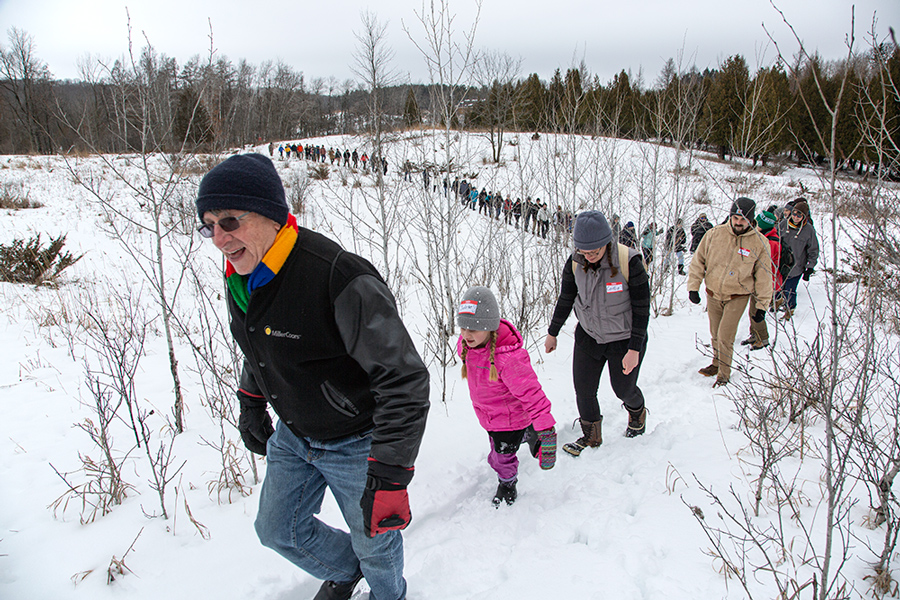 a long line of people hiking up a hill in winter