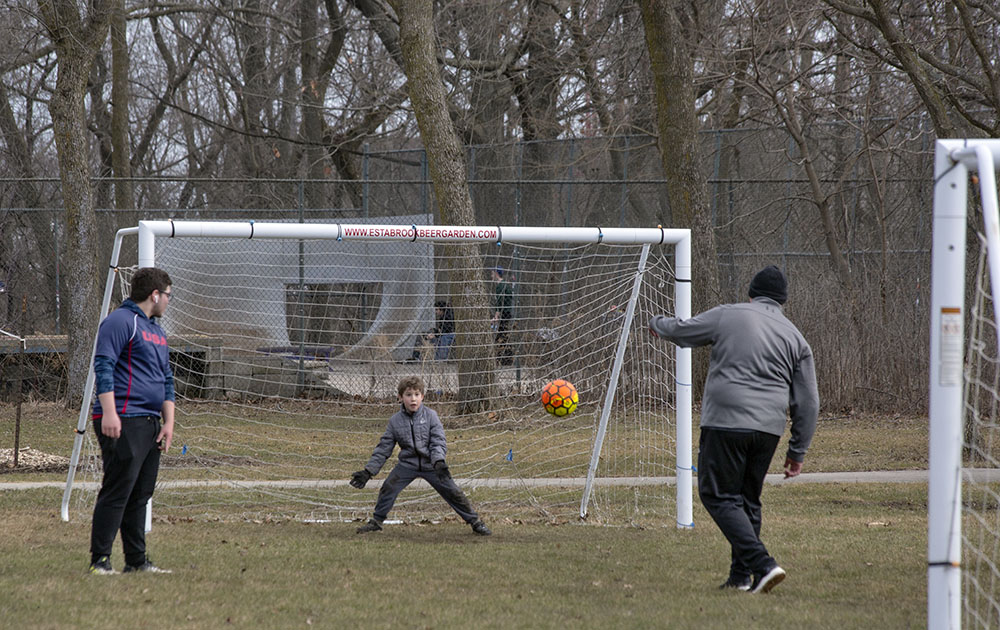 Two young men and a boy playing soccer at Estabrook Park