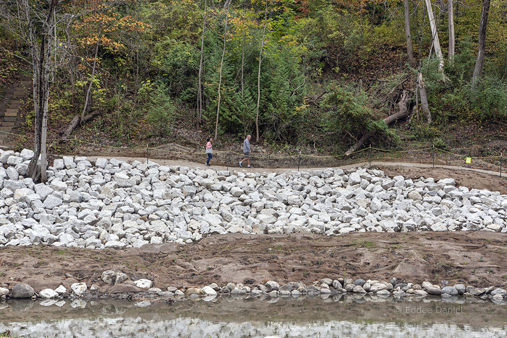 Newly installed rip rap boulders protect a slope; rip rap is a permanent layer of large stones used to armor, stabilize, and protect the soil against erosion. Vegetation will eventually grow up through the stones and along the stream bank, making it look more natural.