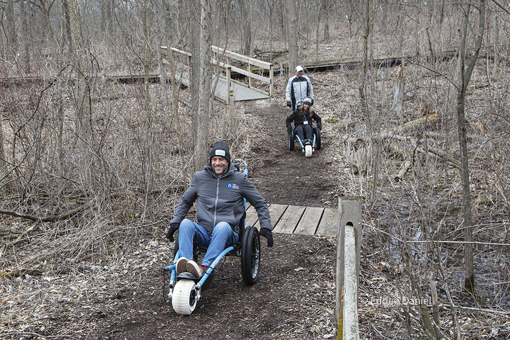 Damian Buchman, Executive Director of The Ability Center out in front on a non-motorized all-terrain wheelchair.