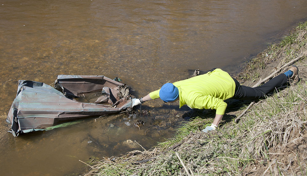 A man on shore reaches for a large, metal object in the Menomonee River.