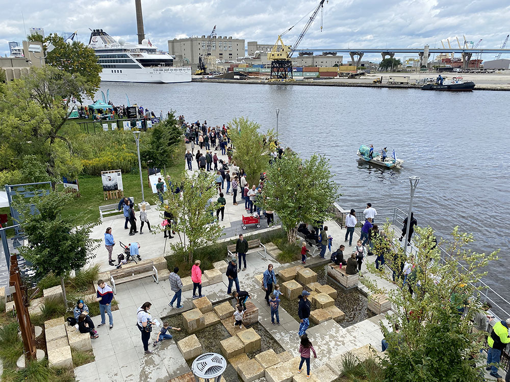 The Milwaukee Riverkeeper boat leads the Boat Parade past Harbor View Plaza where visitors line the waterfront for viewing.