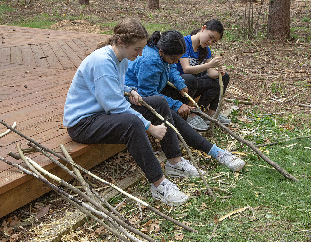 Carving the bark off of birch wood to create walking sticks.