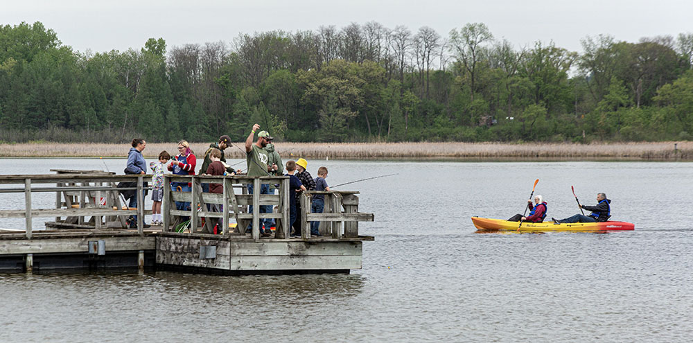 A pier crowded with people fishing and a kayak in Ottawa Lake