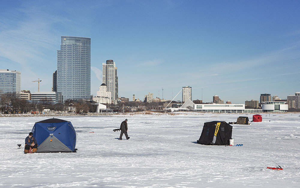 The figure striding across the ice adds scale to the subject of ice fishing shanties. 