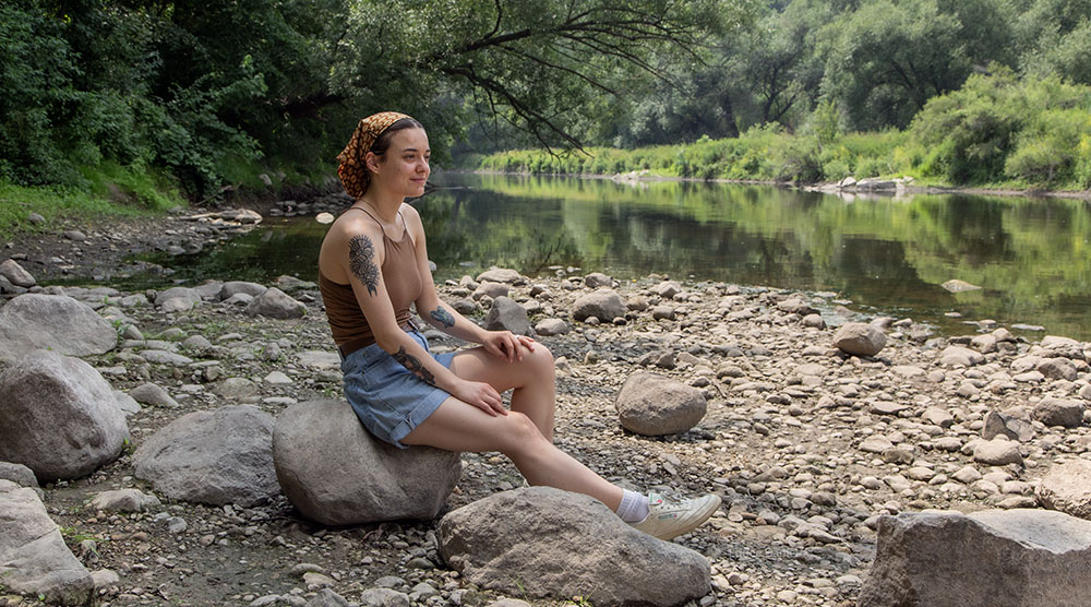 Artist in Residence Haley Krob sitting next to the Milwaukee River