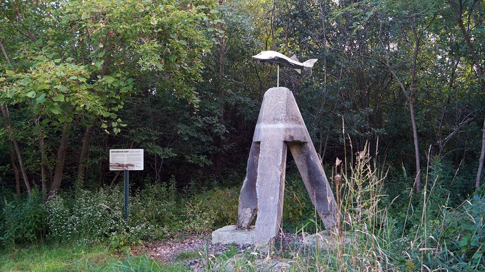 A silvery stainless steel sturgeon sculpture by Milwaukee artist Tom Queoff adorns a relic from the Estabrook Dam on the west bank of the Milwaukee River near Estabrook Falls.