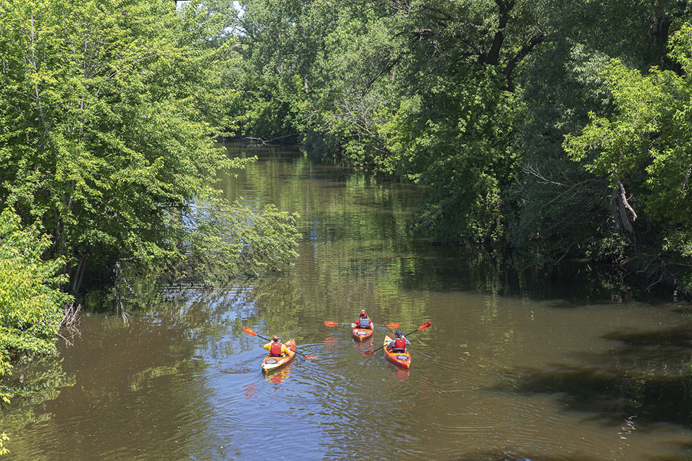 At the upper reaches of the estuary, a trio of kayakers on the Menomonee River at the Three Bridges Park's Valley Passage Bridge.