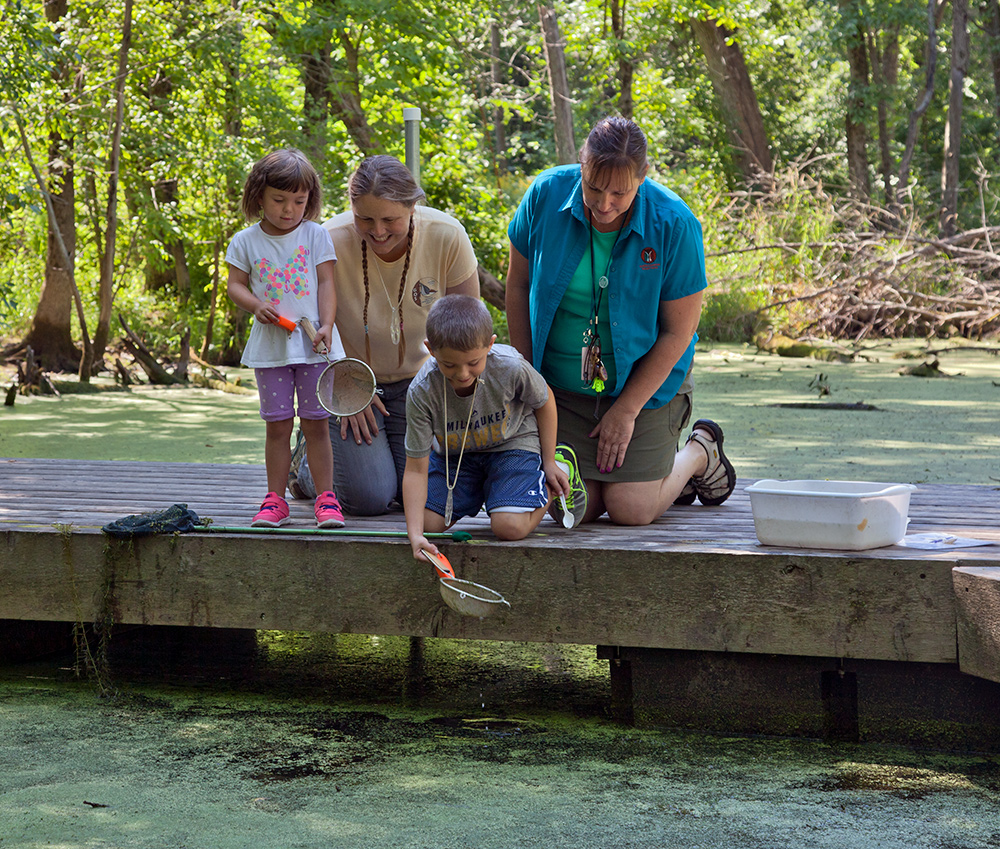 A Schlitz Audubon staff member and Mom look on as a couple of youngsters see what they can find in Turtle Pond.