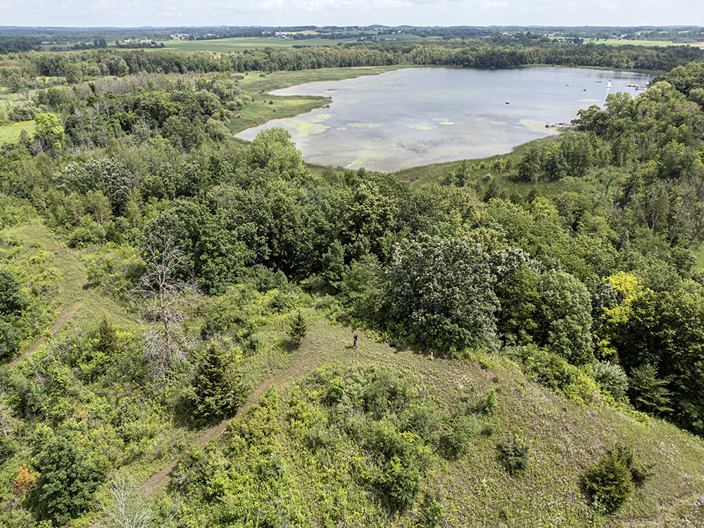 Aerial view of Biehl showing the artist atop the kame in the foreground and Lake 12 in the background. 