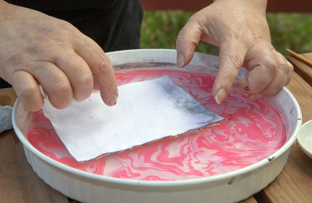 Placing a piece of paper onto the surface of the water/ink.