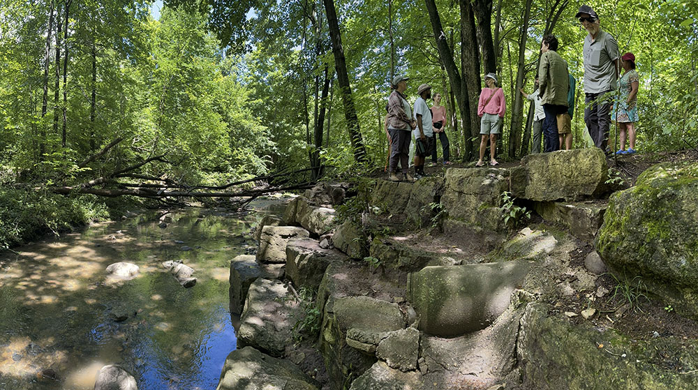 The group overlooks the KK River atop erosion-control stone blocks lining the river bank.