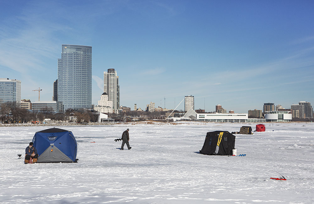 An ice fisherman carrying an ice auger between ice shanties at Lakeshore State Park.