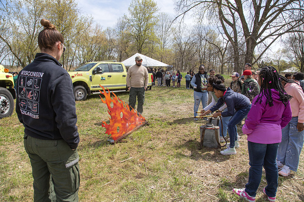 Using actual wildfire fighting equipment, kids spray an artificial blaze.